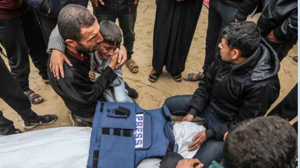১৬ জানুয়ারি, ২০২৫ তারিখে দক্ষিণ গাজার খান ইউনিসের নাসের হাসপাতালে ইসরায়েলি ড্রোন হামলায় নিহত সাংবাদিক আহমেদ আল-শায়াহর স্বজনরা তার কাফন ঢাকা মরদেহের পাশে শোক প্রকাশ করছেন। ছবি: আল-জাজিরা